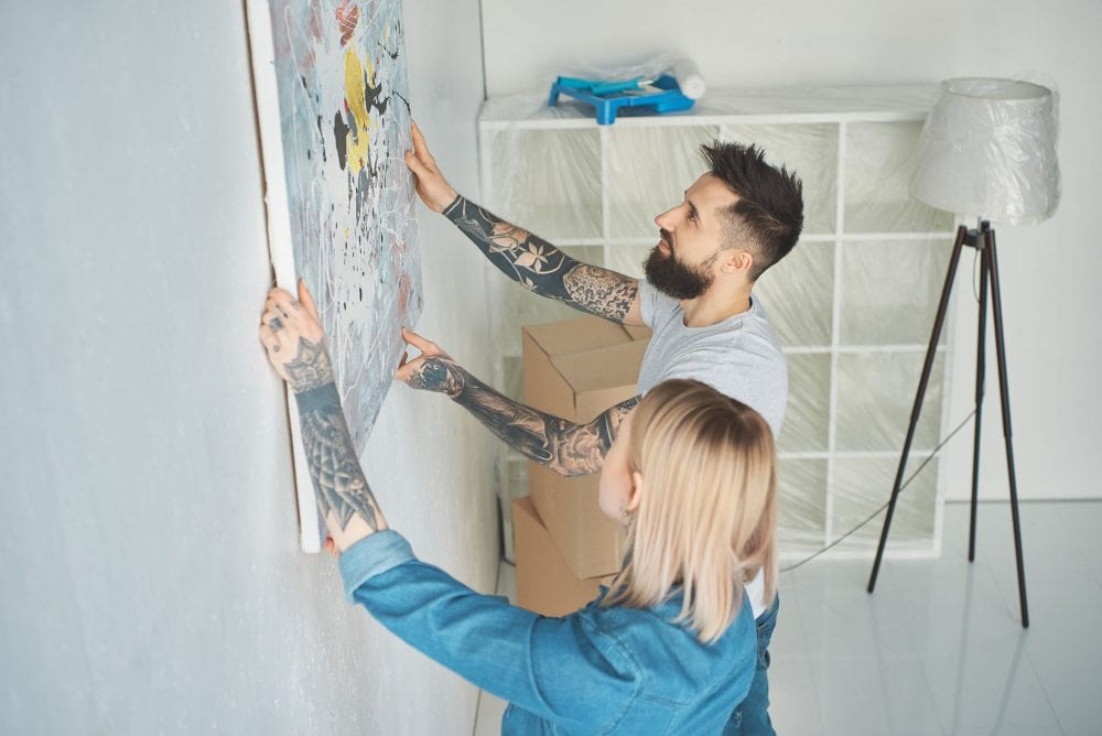 Graphic to show a young couple hanging a painting up in their new home